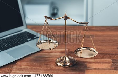 Symbolizing Justice And Legal Authority, Golden Balanced Scale On Desk With Laptop In Law Office Bac