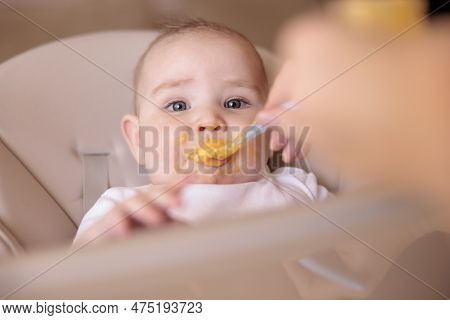 Mother Feeding Porridge To Her Happy Cheerful Baby Boy Using Spoon, Cheerful And Happy Baby Sitting 