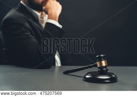 Focus Wooden Gavel Hammer With Burred Background Of Lawyer In Black Suit Sit On His Office Desk, Sym