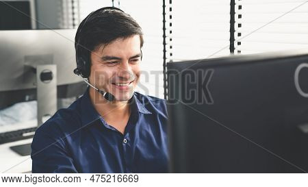Young Competent Asian Male Call Center Agent Working At His Computer While Simultaneously Speaking W