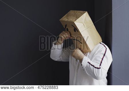 A Sad Man In A White Shirt With A Bag On His Head, With A Drawn Crying Emoticon, Stands Against The 