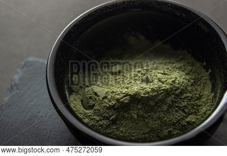 Green Powder In A Small Ceramic Bowl, On A Stone Stand, On A Black Background.  Super Food Or Mariju