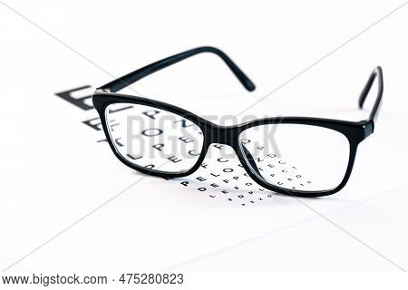 Eyeglasses With Eye Test Table On White, Optometrist Concept And Eye Test