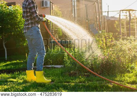 Close Up Woman Gardener In Work Clothes Watering The Beds In Her Vegetable Garden On Sunny Warm Summ