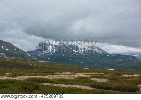 Dramatic Alpine Landscape With Snowy Mountains In Gray Low Clouds. Bleak Atmospheric Scenery Of Tund