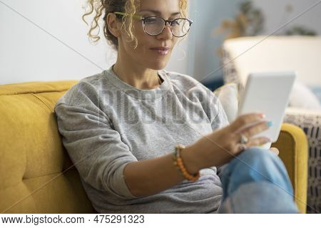 Attractive Middle Age Woman Portrait At Home Reading Book On Ereader Modern Device Witting Comfy On 
