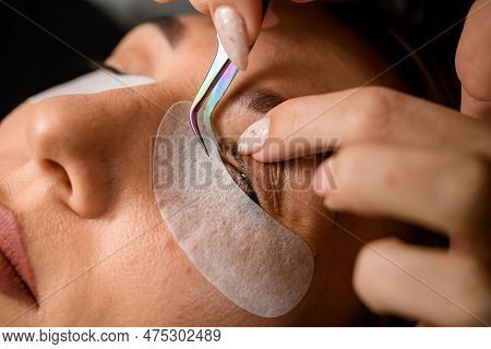 Close-up Of The Female Eyelid And Eyelashes That Beautician Corrects With Tweezers. Eyelash Extensio