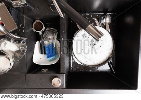 Washing Dishes Concept. Dirty Dishes With Foam From Detergent In A Black Stone Sink In The Kitchen T