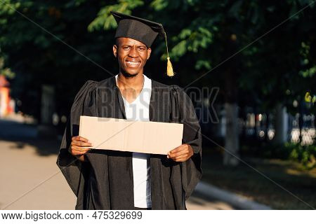 Portrait Of Rejoicing Black Guy Standing With Empty Cardboard Poster On Street In Sunny Day Looking 