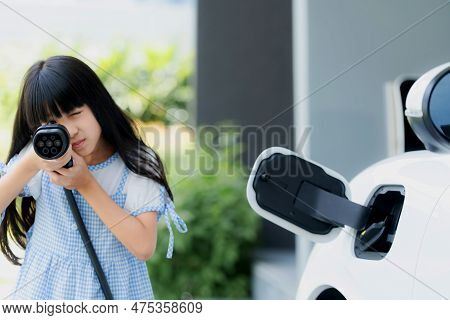 A Playful Girl Holding And Pointing An Ev Plug, A Home Charging Station Providing A Sustainable Powe