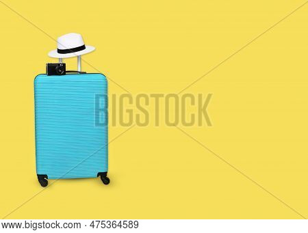 Blue Polycarbonate Suitcase With Hat And Camera On Isolated Yellow Background, Travel And Vacation C
