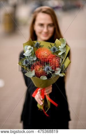 Young Florist Girl Gives To Cameraman Bouquet Of Beautiful Thistle, Leucospermum, Eucalyptus.