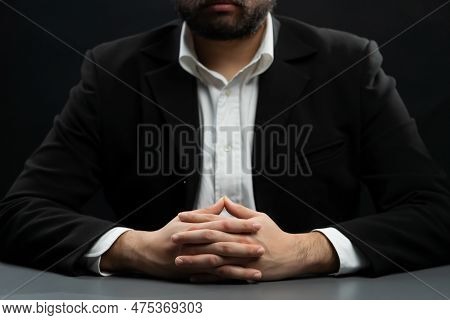 Businessman Or Lawyer Wearing Formal Black Suit Sitting At Table On Isolated Black Background. Conce