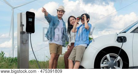 Concept Of Progressive Happy Family Enjoying Their Time At Wind Farm With Electric Vehicle. Electric