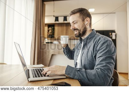 A Happy Remote Worker Is Enjoying Work And His Coffee While Typing On A Laptop.