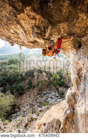 Girl Climber On An Overhanging Rock. A Sports Woman Climbs A Rock Against The Backdrop Of Mountains.