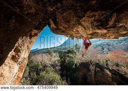 Girl Climber On An Overhanging Rock. A Sports Woman Climbs A Rock Against The Backdrop Of Mountains.