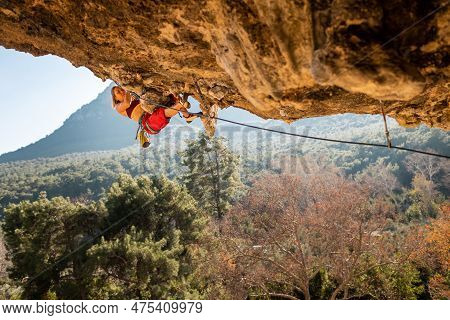A Young Rock Climber On An Overhanging Cliff. The Climber Climbs The Rock. The Girl Is Engaged In Sp