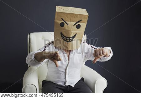 A Man With A Paper Bag On His Head, With An Evil Smiley Face Drawn, Sits On A White Chair, Gloats Em