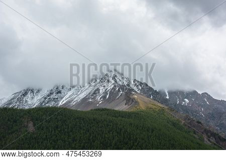 Dark Atmospheric Landscape With Forest Snow Mountain In Low Clouds. Gloomy Overcast Scenery With Hig