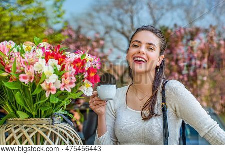Beautiful Woman On A Cafe Enjoying Morning With Cup Of Coffee. She Holds A Cup, Laughing, Spring Flo