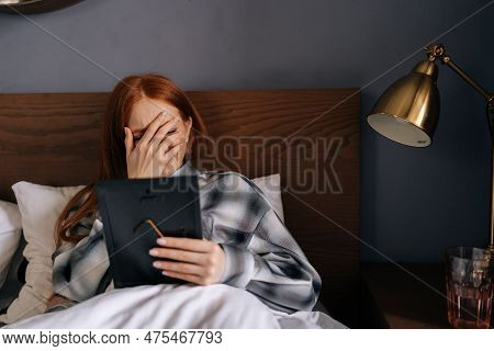 Portrait Of Grief-stricken Young Woman Lying On Bed Covering Face With Hand And Crying While Holding