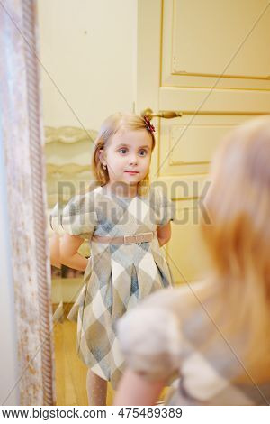 A Cute Little Girl In A Plaid Dress Looks In The Mirror And Primping.