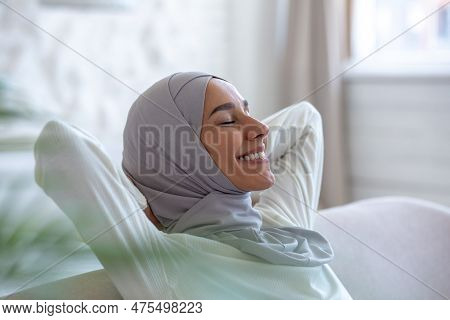 Close-up Photo. Smiling Muslim Young Woman In Hijab Sitting On Sofa At Home And Resting, Eyes Closed
