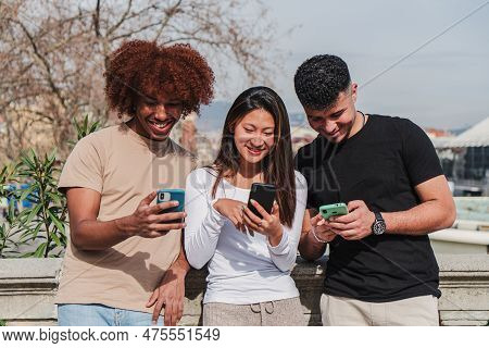 Group Of Multiracial Teenage Friends Having Fun Using A Cellphone Device Outdoors. Three Multiethinc