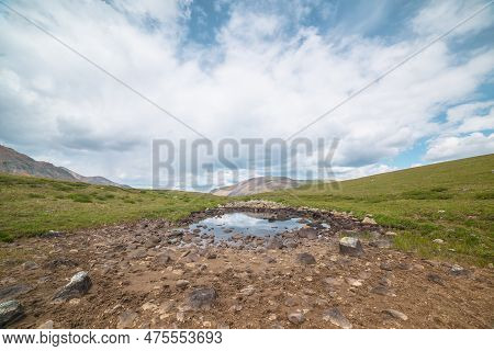 Scenic Alpine Landscape With Small Mountain Lake On Green Grassy Hill Under Cloudy Sky. Dramatic Mou