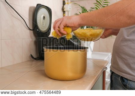 The Man Puts The Potatoes Cut Into Thin Slices Into Bowl Of Slow Cooker. Multicooker. Cooking Lunch 