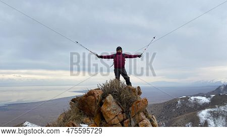 Lonely Tourist Stands On Top Of A Mountain With Trekking Poles Raised Up. View From The Height Of La