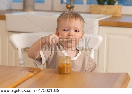 Happy Family At Home. Baby Boy Feeding Himself In Kitchen. Little Boy With Messy Funny Face Eats Hea