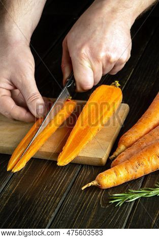 Cook's Hands Cut With A Knife Cut Fresh Carrots On A Wooden Cutting Board. Close-up Of Chef Hands Wh