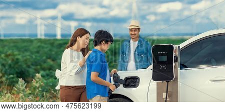 Concept Of Progressive Happy Family Enjoying Their Time At Wind Farm With Electric Vehicle. Electric