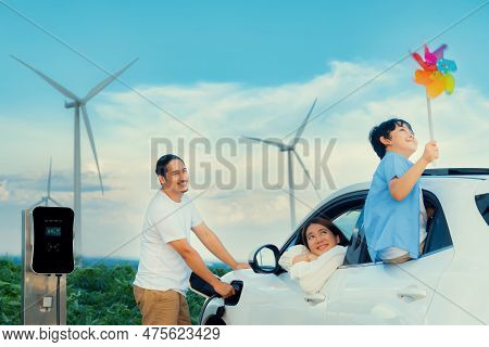 Concept Of Progressive Happy Family Holding Windmill Toy And Relax At Wind Farm With Electric Vehicl