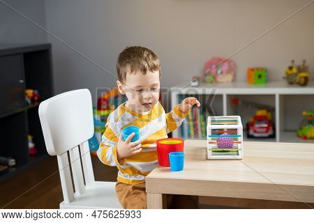 A Cute Little Toddler Boy Of Two Years Old Sits At A Children's Table And Plays With Educational Toy