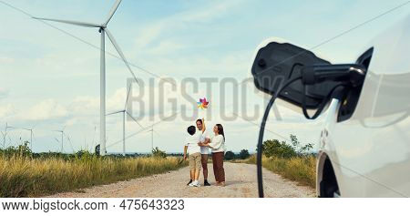 Concept Of Progressive Happy Family Holding Windmill Toy And Relax At Wind Farm With Electric Vehicl