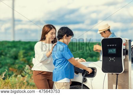 Concept Of Progressive Happy Family Enjoying Their Time At Wind Farm With Electric Vehicle. Electric