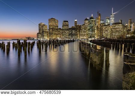 View Of Lower Manhattan At Dusk Seen From Brooklyn. Remaining Of An Old Pier Can Be Seen At The Fore
