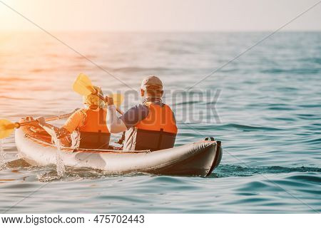 Happy Couple Kayaks In An Inflatable Kayak On The Sea At Sunset. Couple Kanoeing In The Sea Near The