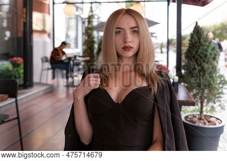 Portrait Of Sexy Young Woman With Blonde Hair And Black Suit With Sweetheart Neckline In Cafe Looks 