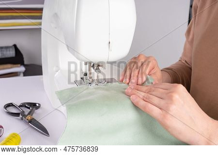Female Hands Stitching White Fabric On Modern Sewing Machine At Workplace In Atelier. Women's Hands 