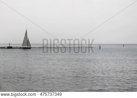 A Seascape Scene With A Sailboat And People On Boards.