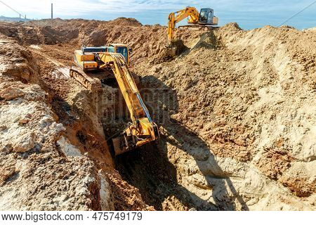 Two Excavator Are Digging Soil In The Construction Site On Sky Background,with White Fluffy Cloud