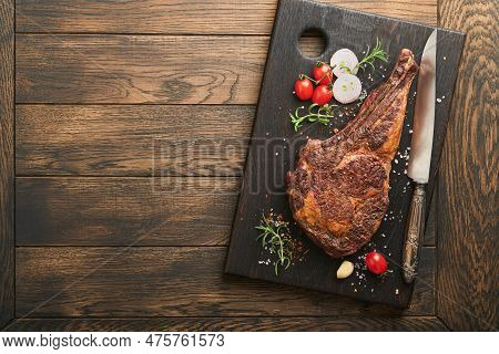 Tomahawk Steak. Sliced Grilled Tomahawk Beef Steak With Baked Cherry Tomatoes, Herbs And Salt On Old
