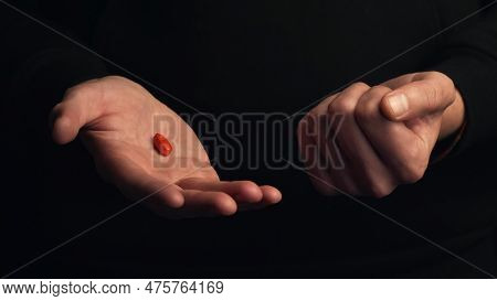 Studio Shot Male Hands Show Red Pill Isolated On Black Background. Concept Of Making Right Choice.