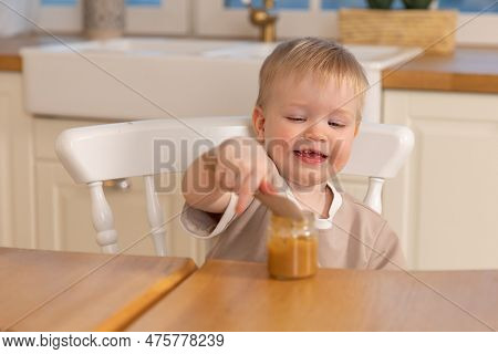 Happy Family At Home. Baby Boy Feeding Himself In Kitchen. Little Boy With Messy Funny Face Eats Hea