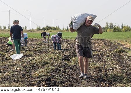 A Cheerful,strong Young Village Man Carries A Bag Full Of Potatoes On His Shoulders,against The Back