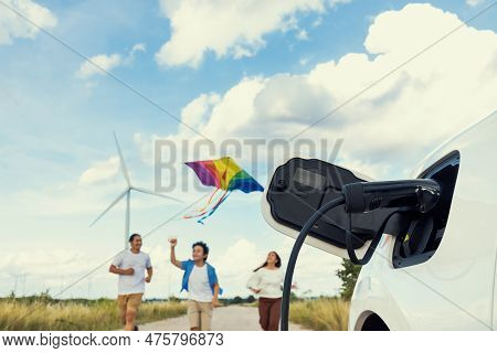 Concept Of Progressive Happy Family Holding Windmill Toy And Relax At Wind Farm With Electric Vehicl